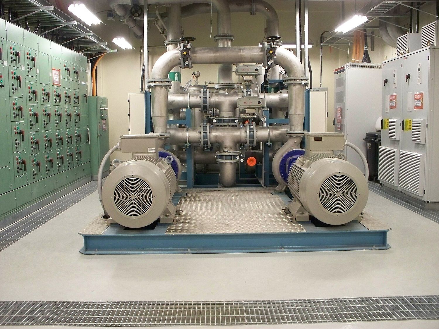 Cuarto de bombeo industrial con dos motores eléctricos acoplados a bombas y un centro de control de motores al fondo.