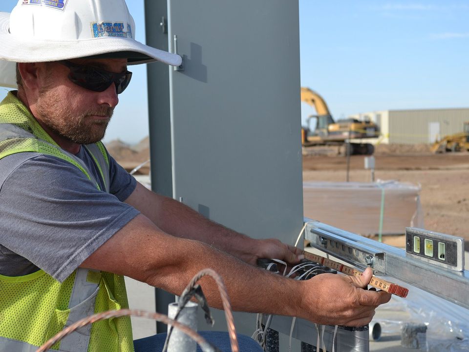 Electricista con chaleco de alta visibilidad conectando conductores en un gabinete de una planta en construcción.
